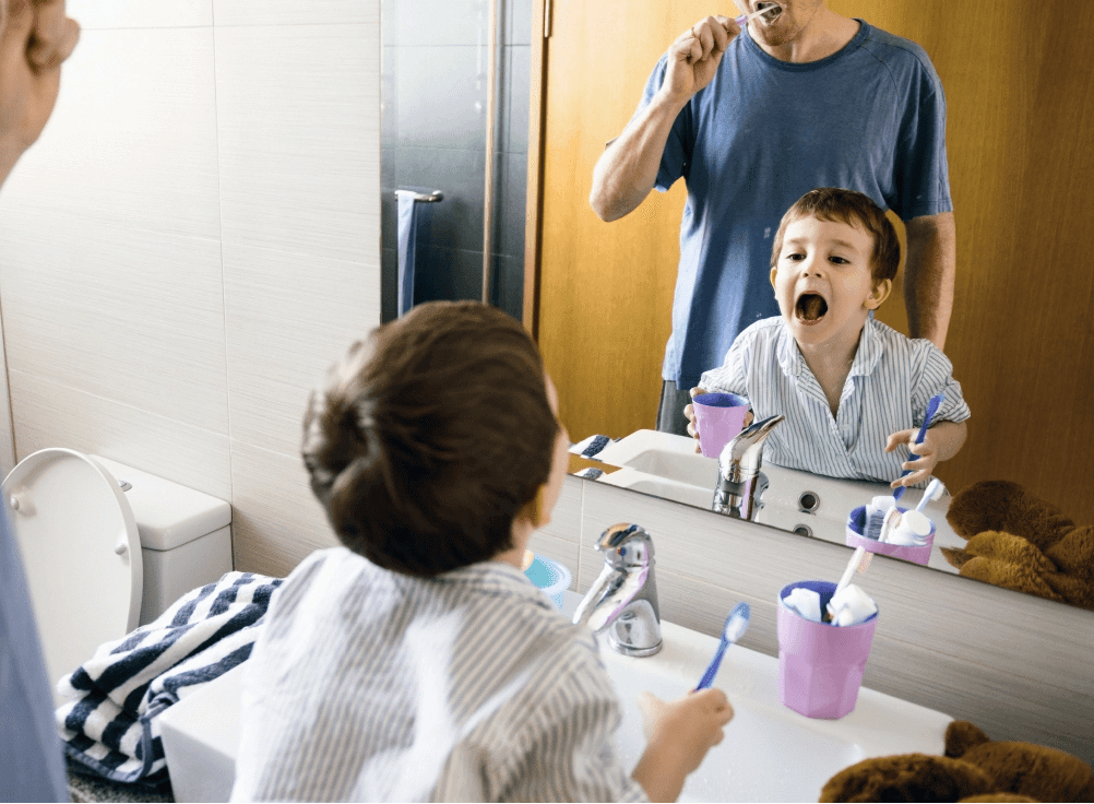 A young boy brushing his teeth with his father.